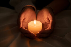 hands gently cradle lit candle casting warm reflective glow darkness